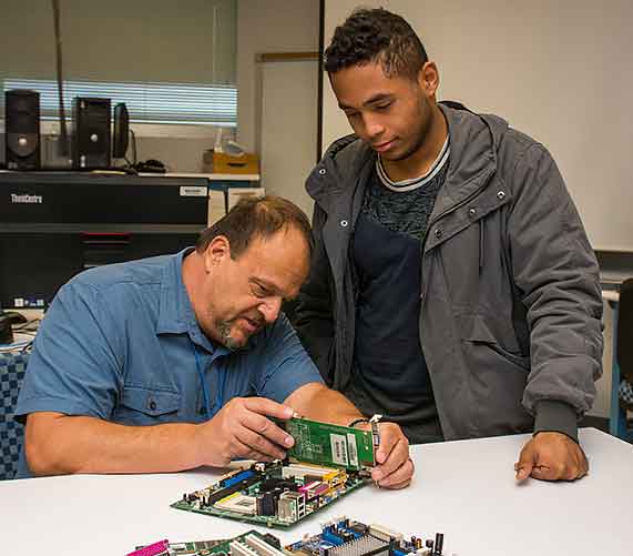 Computer instructor shows student how to work on an internal computer board.