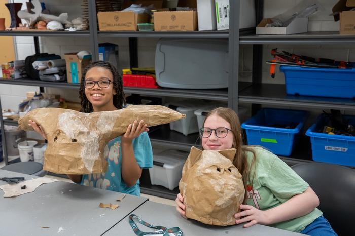 Two paper mache students holding up their paper mache creations