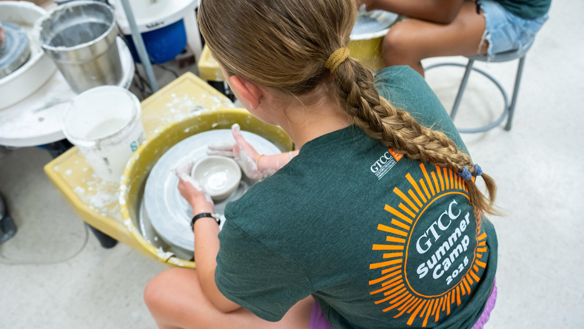 Camper making clay pot and wearing GTCC summer camp T-shirt