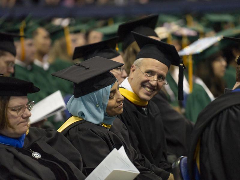 Seated faculty members smile before the start of commencement.