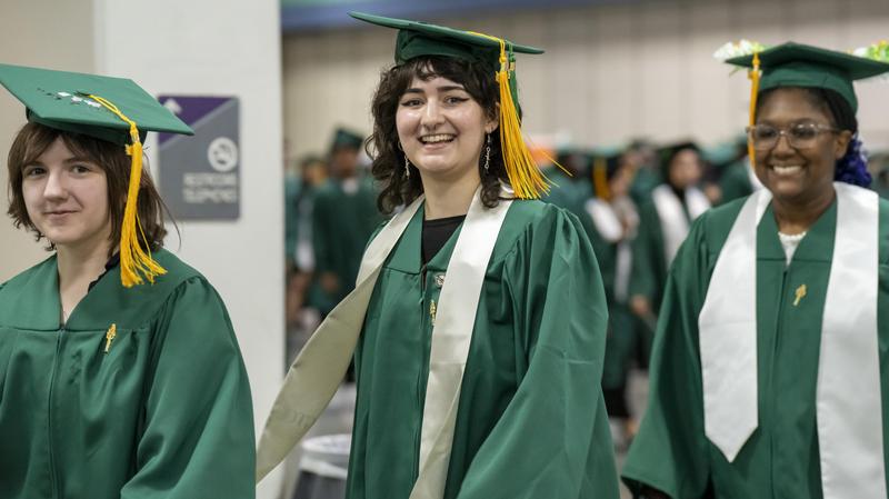 Three female students walk and smile as they prepare backstage for the graduation ceremony.