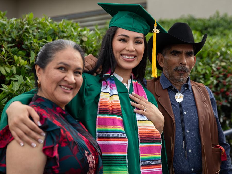 A female graduate, center, her mother, left, and father, right smile after the ceremony.