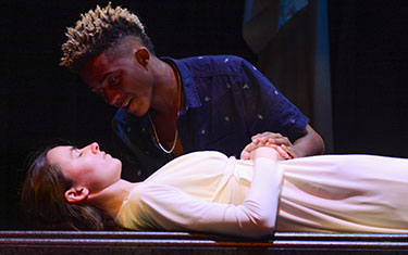 Male student holds sleeping woman's hand in the play Romeo and Juliet.