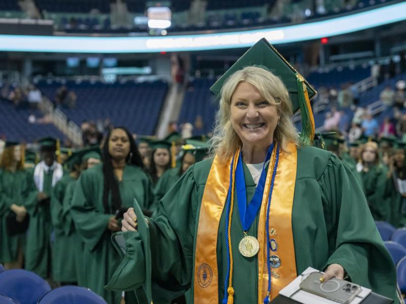 A female students smiles in celebration while wearing two cords.