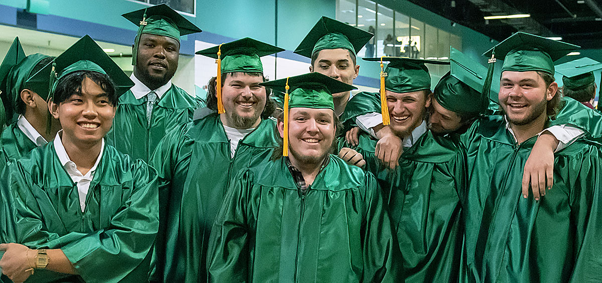 A group of smiling male students pose for a post-graduation picture.