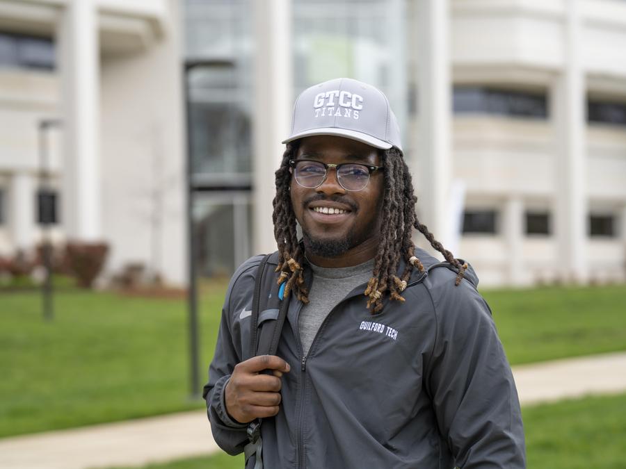 A GTCC student smiles and holds a backpack in front of the Applied Technologies building.