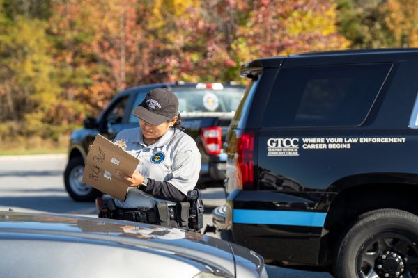 A BLET student writes on a pad between two vehicles.