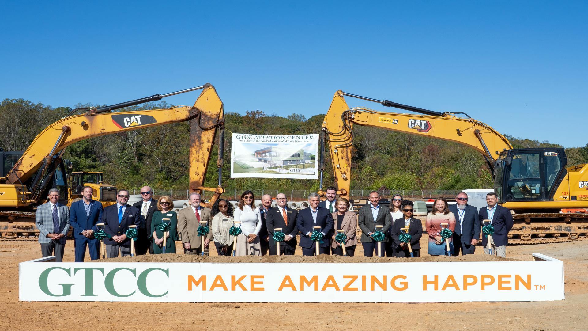 GTCC leaders and partners participate in the Aviation Center groundbreaking ceremony, standing with shovels in front of construction equipment and a banner displaying the future facility rendering.