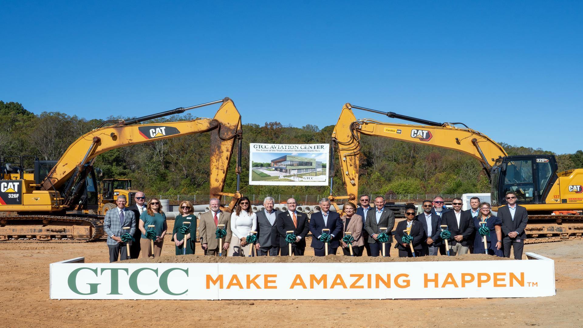 GTCC leaders and partners participate in the Aviation Center groundbreaking ceremony, standing with shovels in front of construction equipment and a banner displaying the future facility rendering.