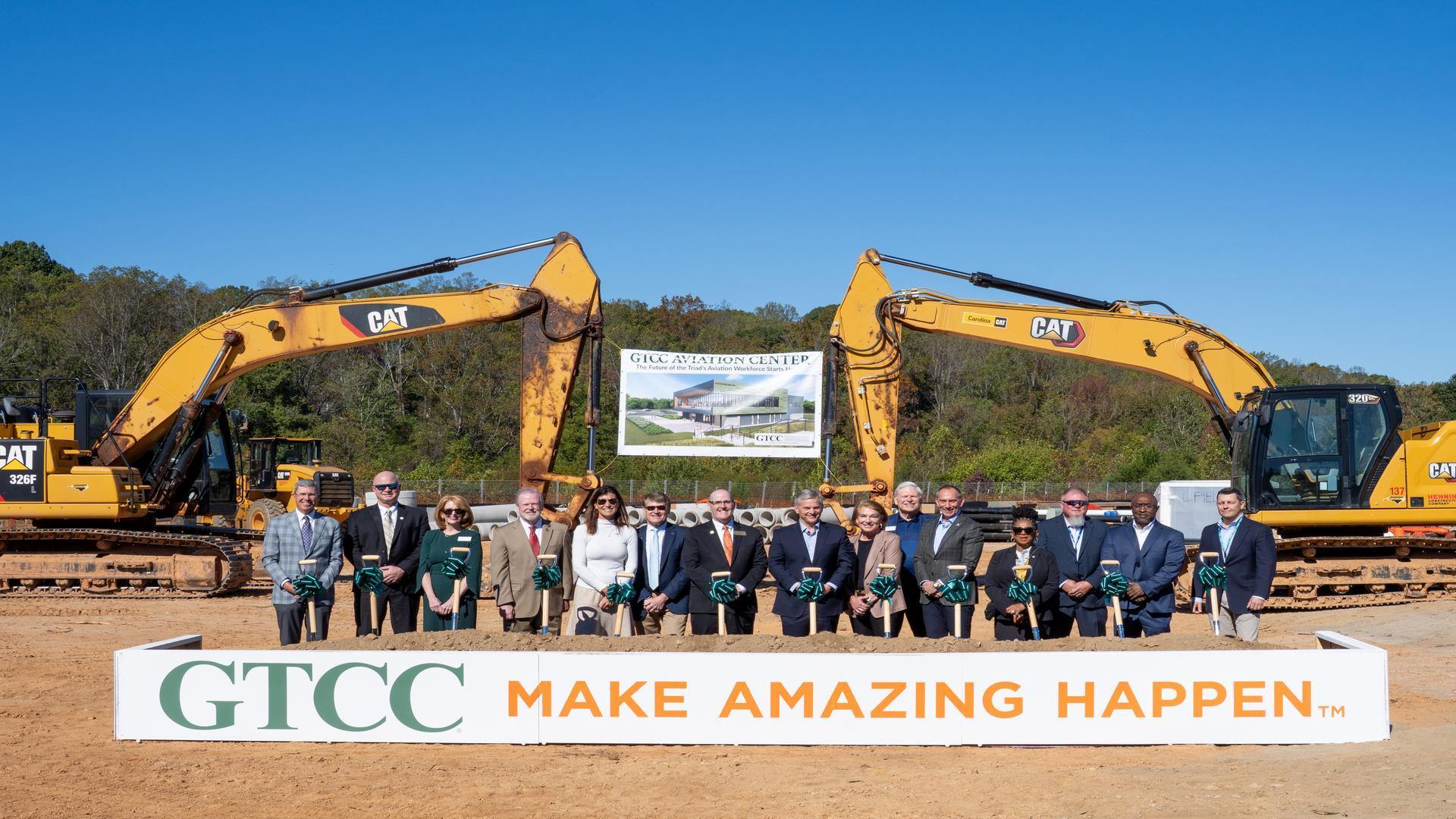 GTCC leaders and partners participate in the Aviation Center groundbreaking ceremony, standing with shovels in front of construction equipment and a banner displaying the future facility rendering.