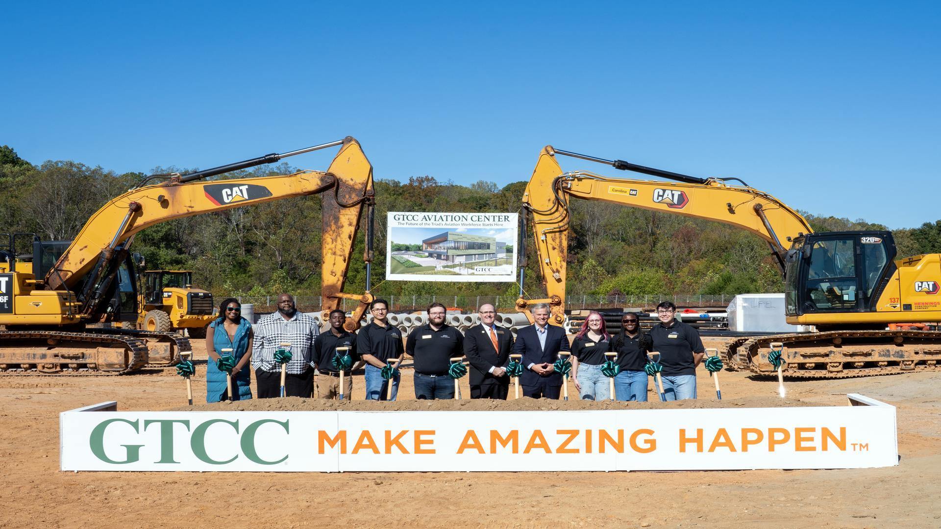 GTCC leaders and partners participate in the Aviation Center groundbreaking ceremony, standing with shovels in front of construction equipment and a banner displaying the future facility rendering.