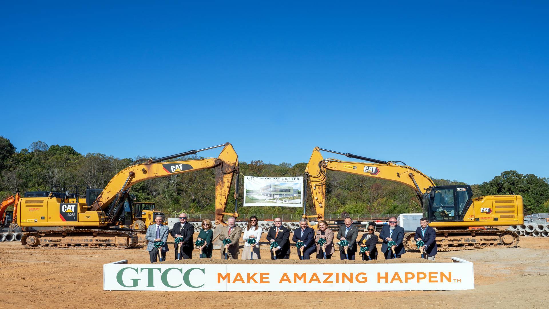 GTCC leaders and partners participate in the Aviation Center groundbreaking ceremony, standing with shovels in front of construction equipment and a banner displaying the future facility rendering.
